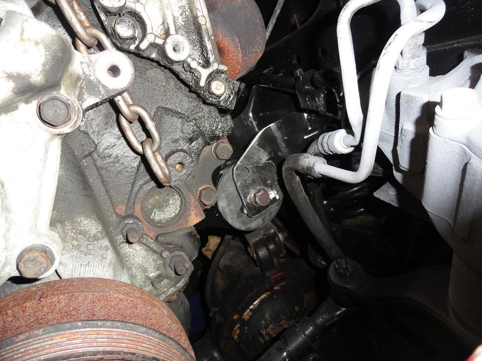 Engine mount with rubber isolator, metal bracket, bolts, and hoses. Chain is attached to engine block
