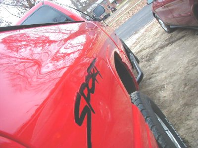 1997 Ford Taurus - A red truck with a "Sport" decal is parked next to another red vehicle.