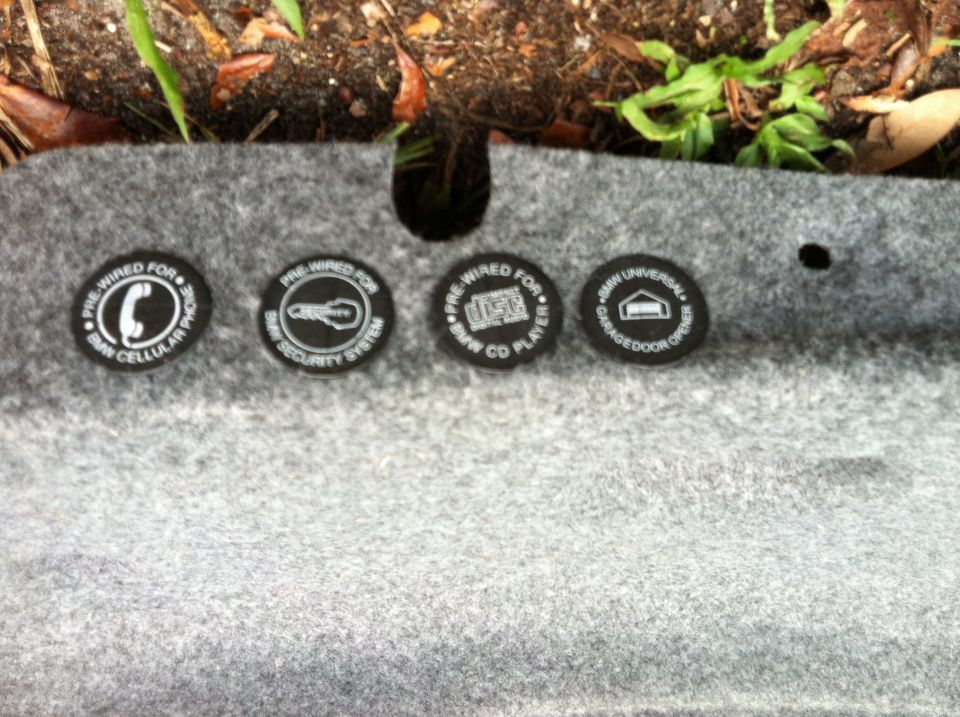 Four circular BMW labels: PRE-WIRED FOR BMW CELLULAR PHONE, PRE-WIRED FOR BMW SECURITY SYSTEM, PRE-WIRED FOR BMW CD PLAYER, BMW UNIVERSAL GARAGE DOOR OPENER