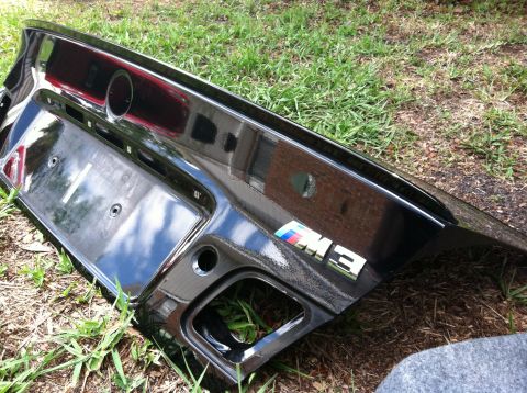 2005 BMW M3 - A black BMW M3 trunk lid is shown resting on grass, the M3 emblem and license plate mounting area.