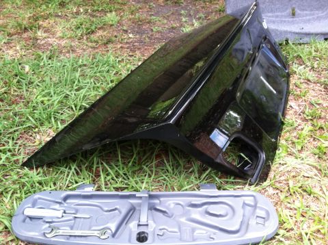2005 BMW M3 - A black car trunk lid and its associated tool kit are displayed on a grassy surface.
