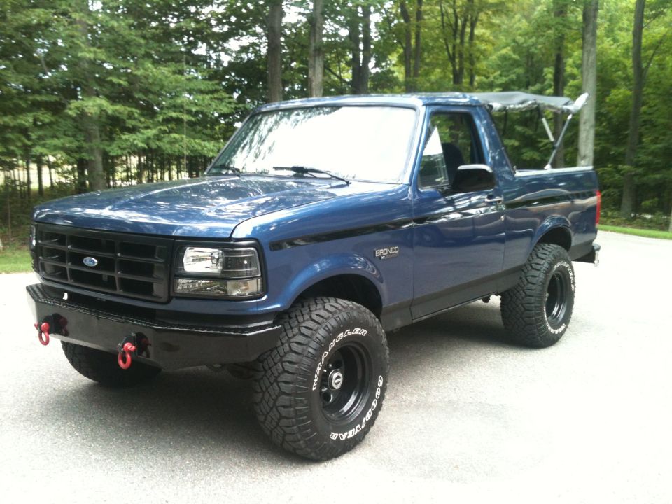 Blue Ford Bronco with aftermarket bumper and off-road tires, viewed from the front three-quarter angle