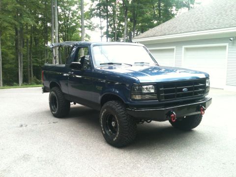 1996 Ford Bronco - A dark blue Ford Bronco is parked in a driveway with a garage in the background.