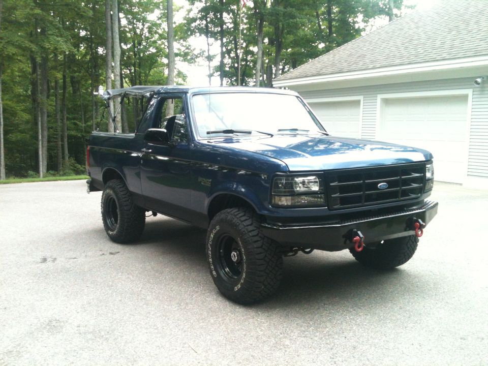 Dark blue Ford Bronco with black grille and aftermarket bumper, lifted with off-road tires