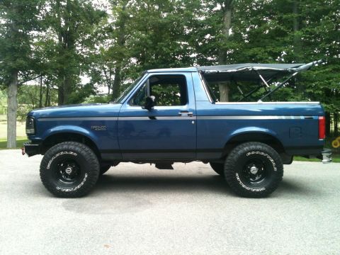 1996 Ford Bronco - Blue two-tone 1996 Ford Bronco shown in side profile with the soft top folded back, riding on a suspension lift with black steel wheels and…