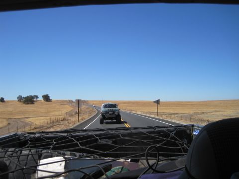 1989 Ford Bronco - Two vehicles travel down a two-lane highway through a dry, grassy landscape under a clear blue sky.