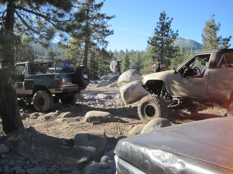 1989 Ford Bronco - Off-road vehicles navigate a challenging, boulder-strewn path in a forest environment.