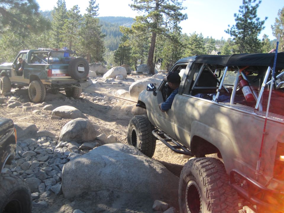 Tan off-road SUV being towed by a green off-road SUV on a rocky trail