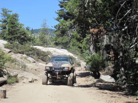1989 Ford Bronco - A tan off-road SUV navigates a rocky trail under a clear blue sky.