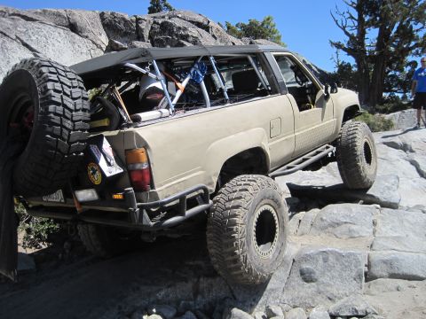 1989 Ford Bronco - This modified SUV navigates a challenging rocky terrain under a clear blue sky.