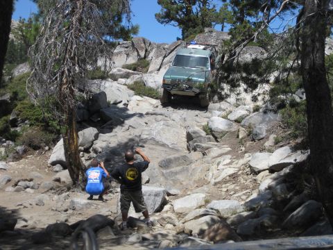 1989 Ford Bronco - An off-road SUV navigates a challenging rocky incline, with onlookers observing the ascent.