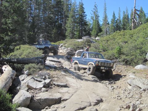 1989 Ford Bronco - Two trucks tackle a challenging rocky trail in a wooded, mountainous area.