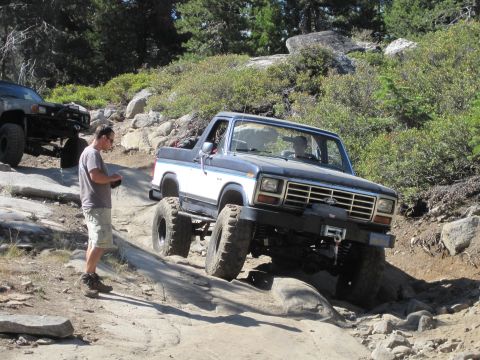1989 Ford Bronco - A modified Ford Bronco tackles a challenging off-road course with another vehicle visible in the background.