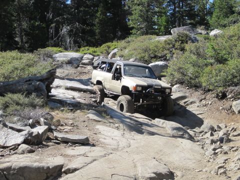 1989 Ford Bronco - Modified Toyota pickup truck tackling a challenging rocky off-road course in a wooded area.