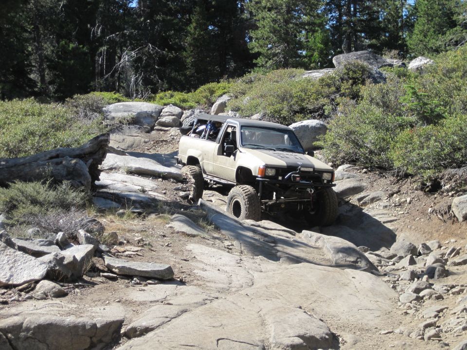 Tan Toyota pickup truck with off-road modifications navigating a rocky trail