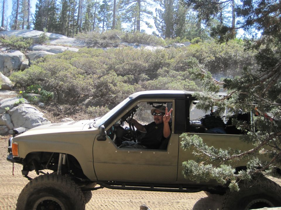 Tan pickup truck with lifted suspension and off-road tires, driver giving peace sign