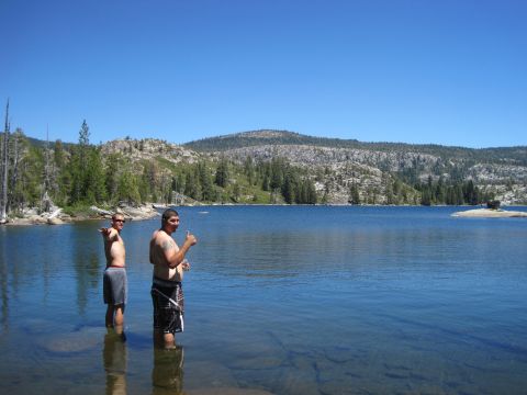1989 Ford Bronco - Two men enjoy a sunny day by wading into a calm lake, with a scenic mountain landscape behind them.