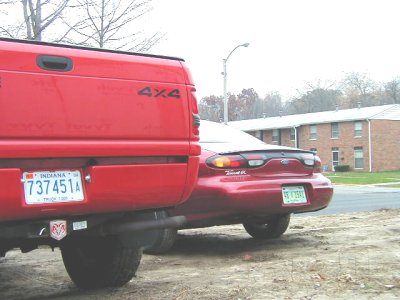 1997 Ford Taurus - Rear view of a 1997 Ford Taurus next to a red pickup truck.