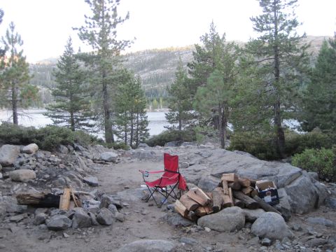 1989 Ford Bronco - A campsite is set up near a lake, with firewood stacked and a chair ready for use.