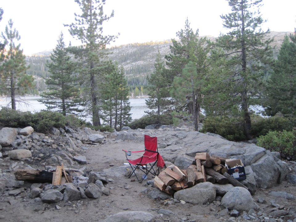 Campsite with a red folding chair, firewood, and a lake in the background
