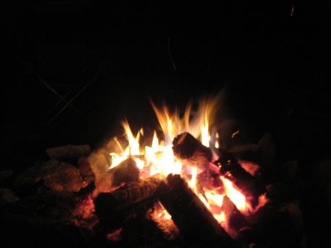 1989 Ford Bronco - A campfire burns brightly at night, illuminating logs and surrounding rocks.
