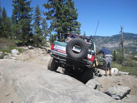 1989 Ford Bronco - A green Ford Bronco is seen off-roading on a rocky trail with a person assisting.