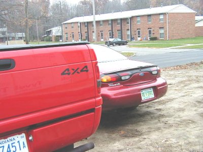 1997 Ford Taurus - A red pickup truck and a red sedan are parked in front of apartment buildings.