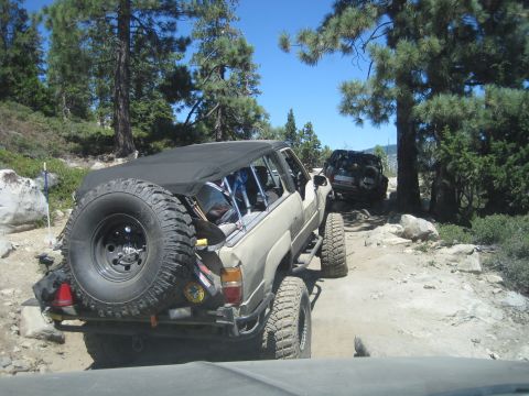 1989 Ford Bronco - Two SUVs navigate a challenging, rocky trail under a clear blue sky.