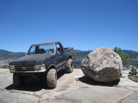 1989 Ford Bronco - A black Ford Bronco with large off-road tires is parked on a rocky surface with a scenic mountain view in the background.