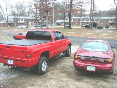 1997 Ford Taurus - A red sedan is parked next to a red pickup truck in a residential area.