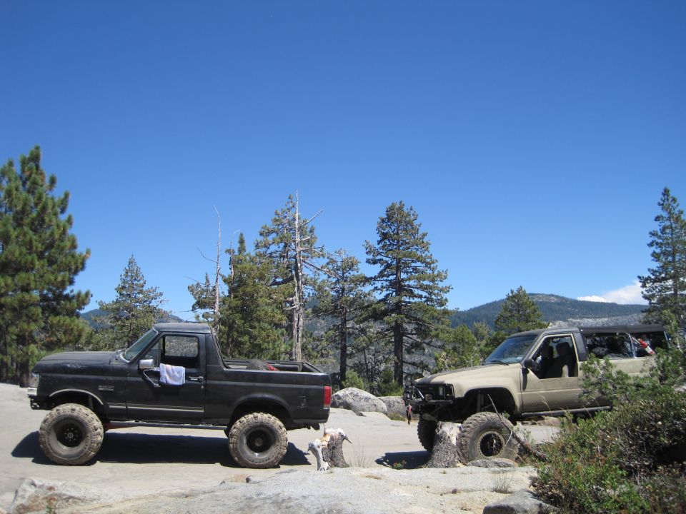 1989 Ford Bronco and a tan Toyota 4Runner modified for off-roading parked on rocks