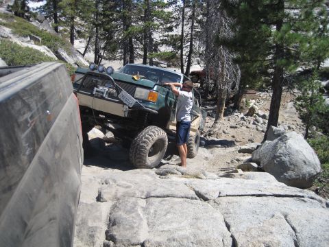 1989 Ford Bronco - A modified green SUV tackles a challenging rocky terrain, with a person observing its progress.