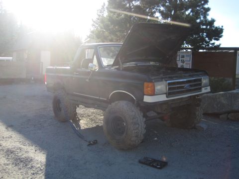 1989 Ford Bronco - A modified black Ford Bronco sits with its hood up, showing off its lifted suspension and off-road tires.