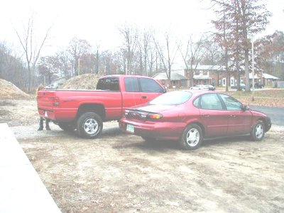 1997 Ford Taurus - A red 1997 Ford Taurus is seen parked next to a red pickup truck on a cloudy day.