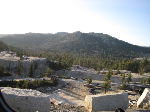 1989 Ford Bronco - A scenic view of a hillside parking area dotted with various vehicles, surrounded by trees and mountains under a clear sky.