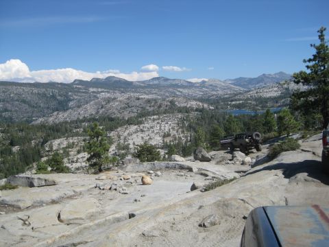 1986 Ford Bronco - Off-road vehicles navigate a mountain landscape under a clear blue sky.