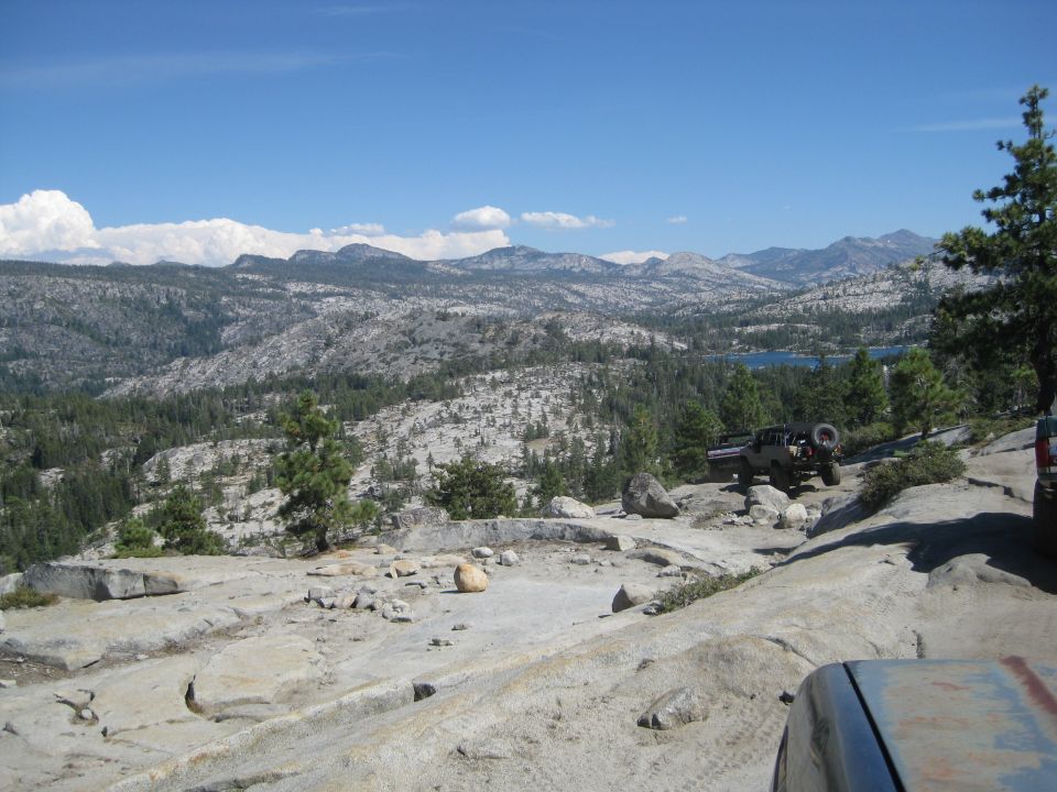 Two off-road vehicles on a rocky mountain trail with a lake in the distance