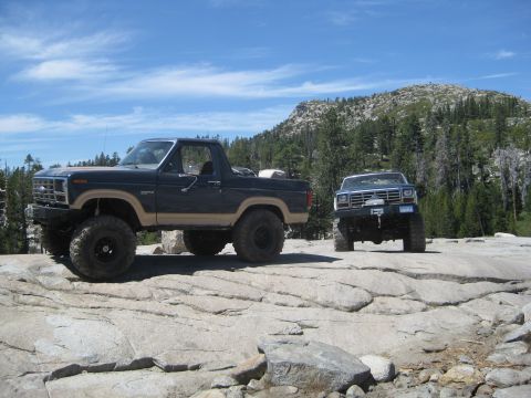1986 Ford Bronco - Two Ford Broncos are parked on a rocky surface in a mountainous area.