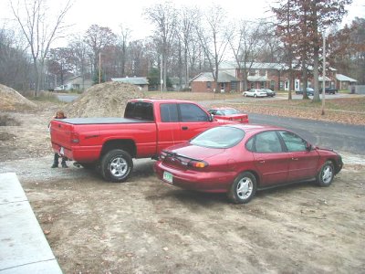 1997 Ford Taurus - Two vehicles, a red Ford Taurus and a red pickup truck, are parked side-by-side on a dirt lot.