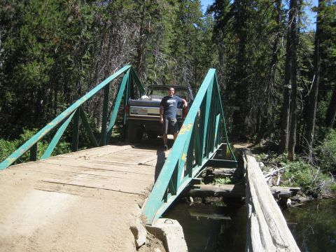1986 Ford Bronco - A man stands next to a brown Ford Bronco on a wooden bridge in a forest.