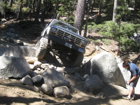 1986 Ford Bronco - This 1986 Ford Bronco is tackling a challenging off-road course with significant rock obstacles.
