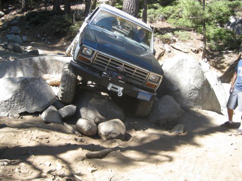 1986 Ford Bronco - This Ford Bronco is shown off-roading through a challenging rocky path in a wooded area.