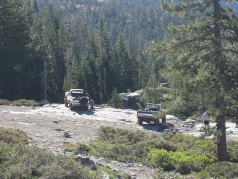 1986 Ford Bronco - Two trucks are parked on a rocky, wooded trail with people standing around them.