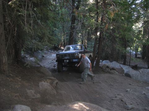 1986 Ford Bronco - A person walks alongside a vintage pickup truck navigating a rocky, wooded trail.