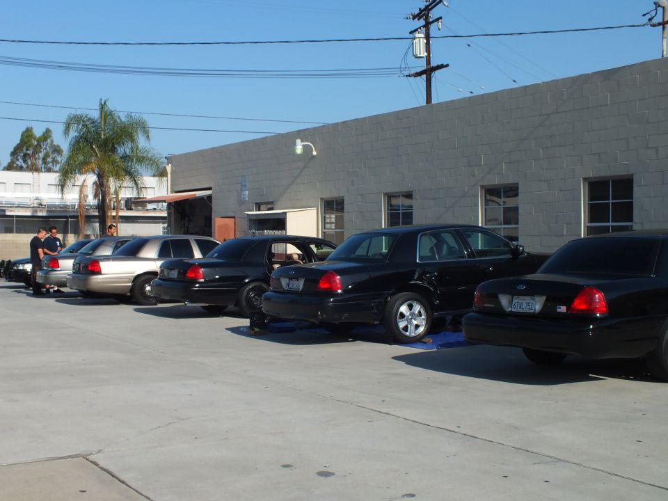 Black and gray Crown Victoria sedans parked diagonally at a gray industrial building, one on ramps