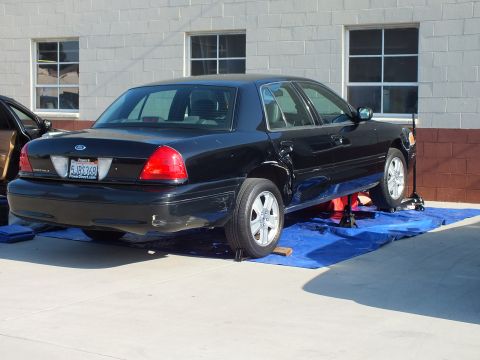 2003 Ford Crown Victoria - Black Crown Victoria on blue alignment mats by a block wall; rear plate 5JBC368, chrome aftermarket wheels.