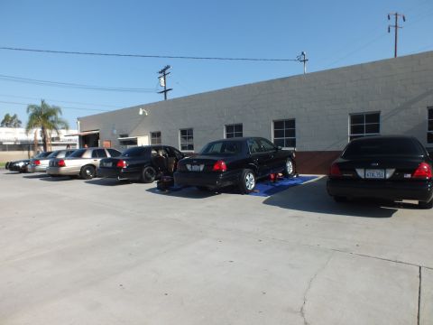 2003 Ford Crown Victoria - Several dark full-size sedans parked at a warehouse; nearest car door open while sitting on blue ramps.