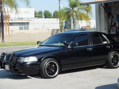 2003 Ford Crown Victoria - Side profile of lowered black Crown Victoria, brush guard and dark tint, parked near open garage bays
