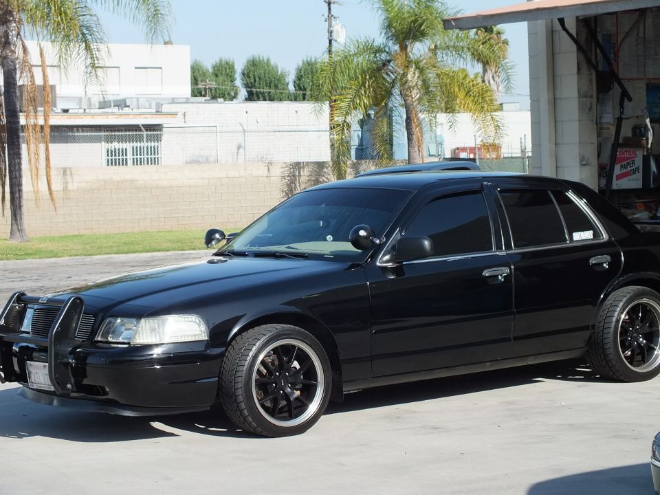 Black Ford Crown Victoria sedan with push bar, sunroof and tinted windows on black wheels at shop