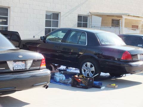 2003 Ford Crown Victoria - Dark Crown Victoria being serviced over a tarp, gray sedan with plate 6CBY698 alongside